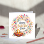 Happy Bandi Chhor Divas greeting card with gold and navy script lettering, colourful firework patterns and a glowing pink and gold diya, displayed with a white envelope