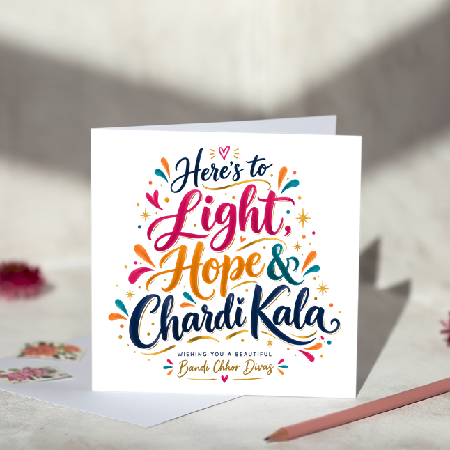Bandi Chhor Divas greeting card reading “Here’s to Light, Hope & Chardi Kala” in colourful script lettering with hearts and gold starbursts, displayed with a white envelope